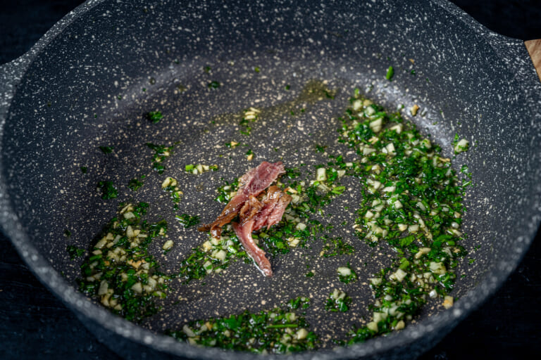 Sautéing herbs with garlic and anchovies in a pan