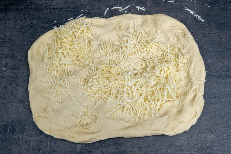 Rolling out the bread dough and sprinkling with cheese Rolling out the bread dough and sprinkling with cheese