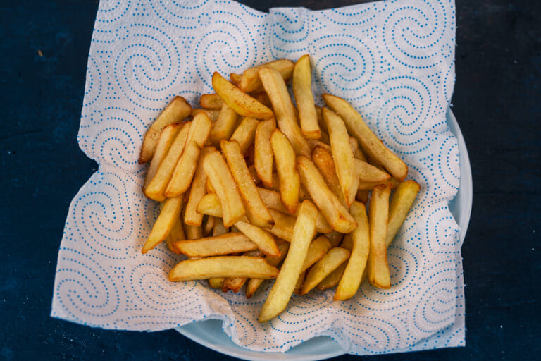 Freshly fried, golden french fries being sprinkled with salt