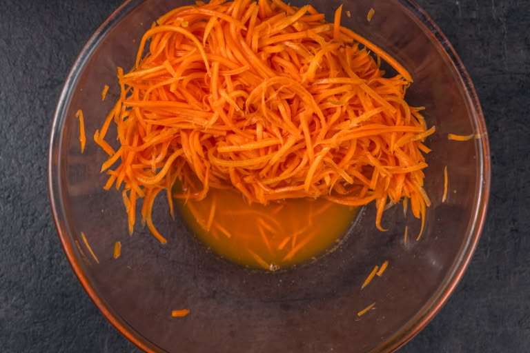 Hands gently squeezing excess juice from the marinated carrots into a bowl.