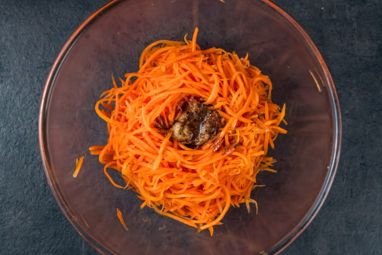 Hot spiced oil being poured directly onto the garlic in the carrot mound, with steam rising.