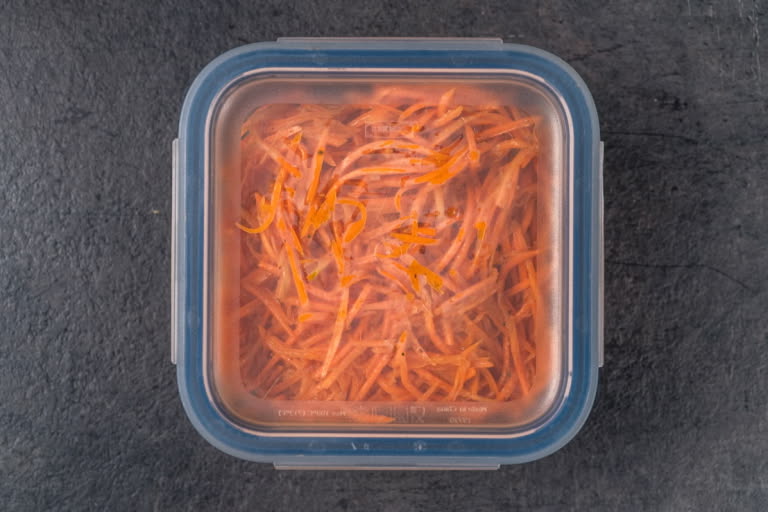 The prepared spicy carrot salad being placed into an airtight glass container for marination.