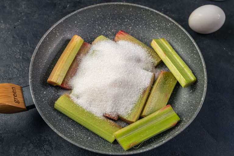 Chopped rhubarb and sugar combined in a large skillet, ready to be caramelized.