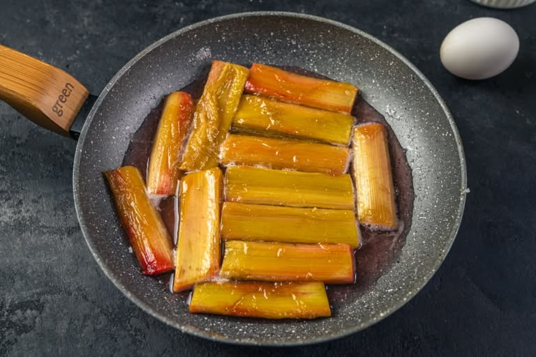 Caramelized rhubarb pieces simmering in their own juices and sugar syrup in a skillet.