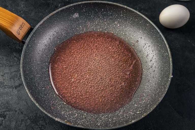 Rhubarb juice being reduced to a thick, bubbling syrup in the skillet.