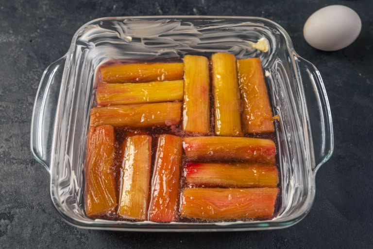 Caramelized rhubarb pieces neatly arranged in the bottom of a square baking pan and covered with syrup.