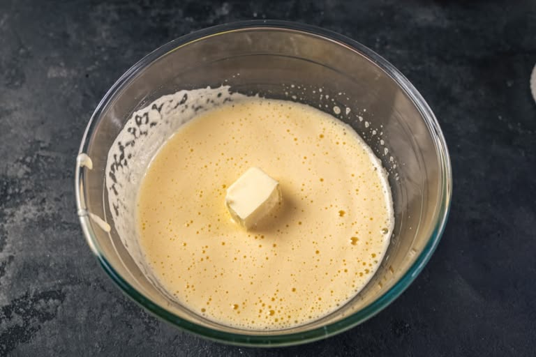 Softened butter being added to the whipped egg and sugar mixture.