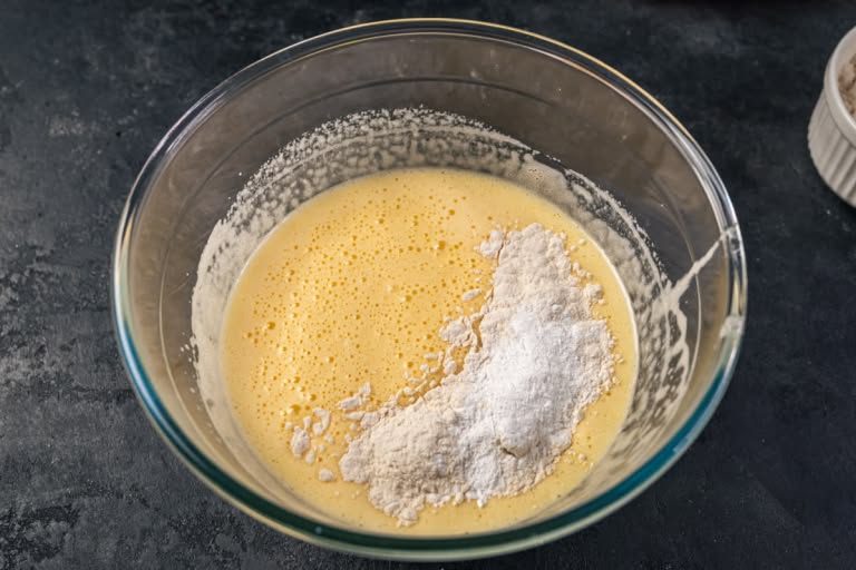 Sifted flour being folded into the cake batter in a glass bowl.