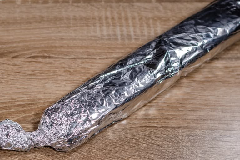 The chocolate salami log tightly wrapped in aluminum foil, with the ends twisted shut like a candy wrapper.