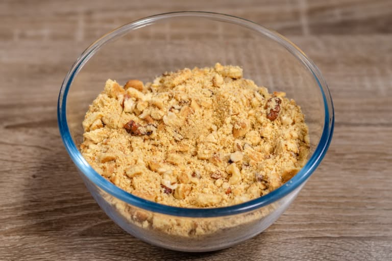 A glass bowl containing a mixture of finely and coarsely crushed cookie crumbs and chopped walnuts.