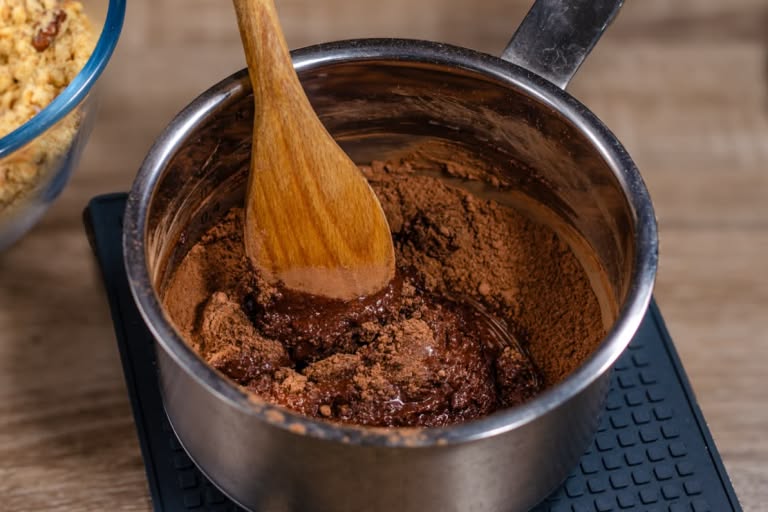 Pouring milk into a saucepan containing a mixture of cocoa powder and sugar.