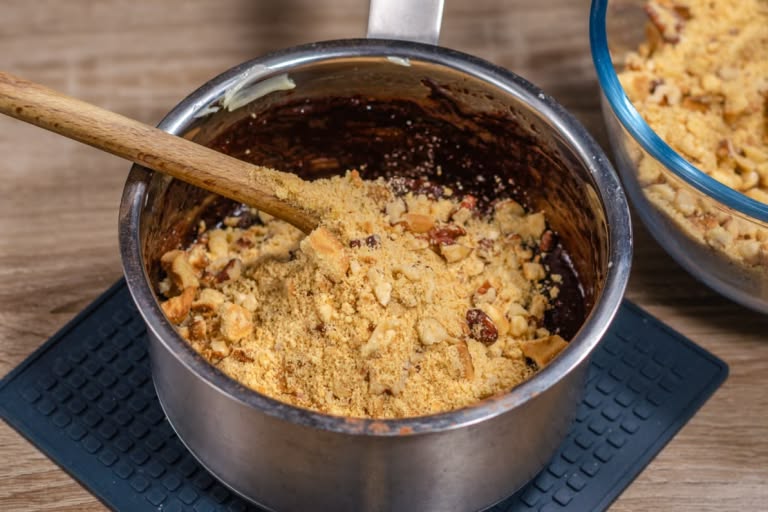 Adding the cookie and walnut crumb mixture to the melted chocolate-butter base.