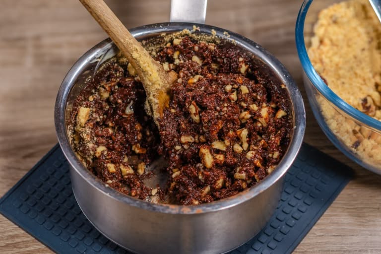 Stirring the final thick, dense mixture of chocolate, cookies, and walnuts with a spatula in a saucepan.