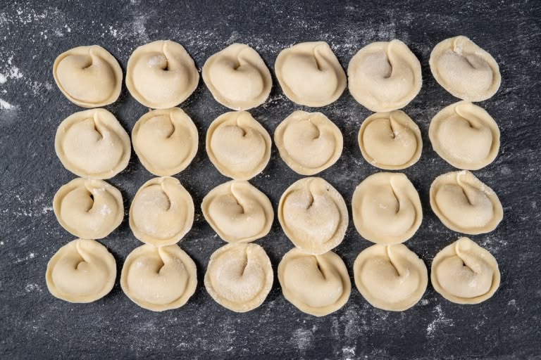Finished uncooked pelmeni arranged on a floured baking sheet
