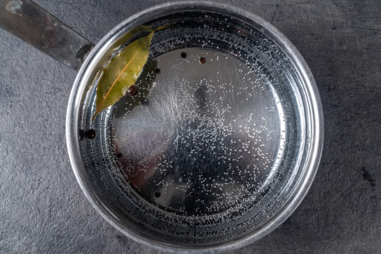 A large pot of water coming to a rolling boil with bay leaves