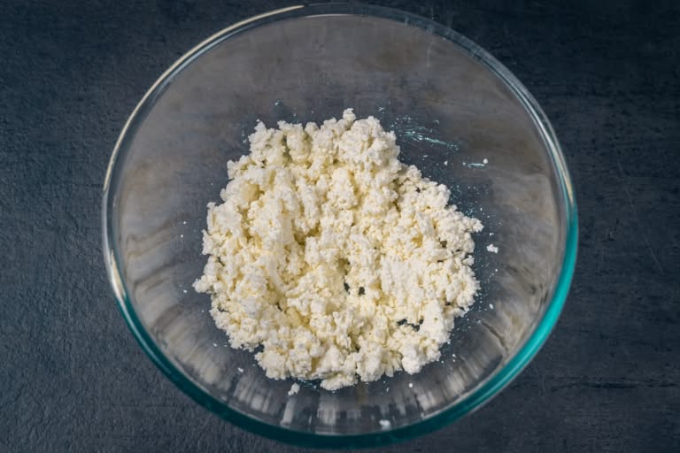 Mashing farmer's cheese with a fork in a white mixing bowl.