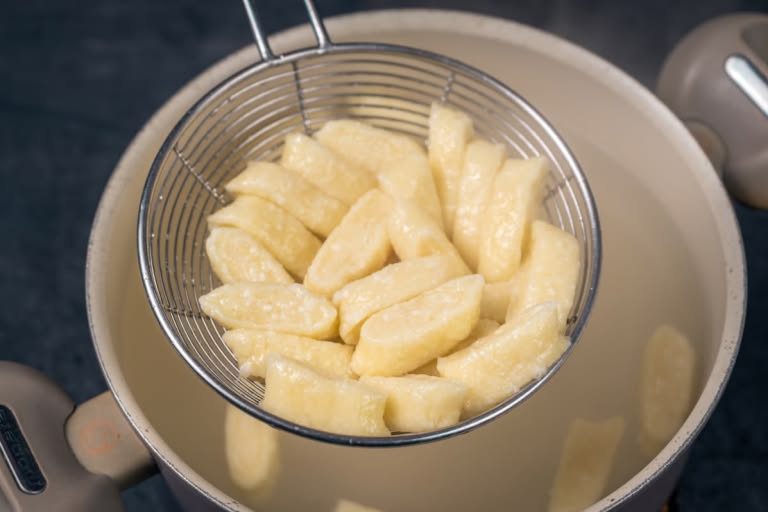 Removing cooked, floating lazy vareniki from the pot with a slotted spoon.