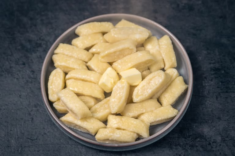Freshly cooked lazy vareniki being tossed with melted butter in a plate.