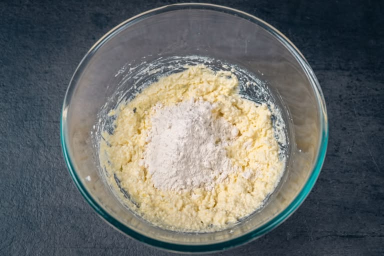 Adding the first tablespoon of all-purpose flour to the cheese and egg mixture.