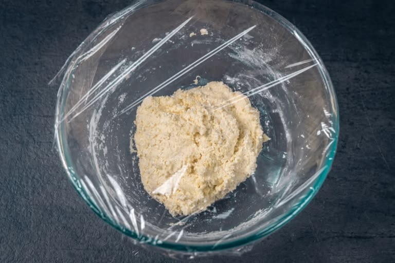 Lazy vareniki dough resting in a bowl covered with plastic wrap.