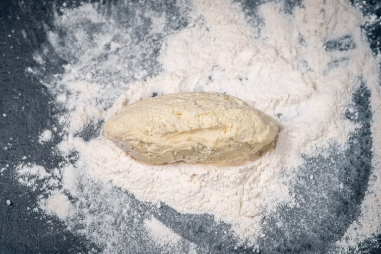 A portion of soft vareniki dough placed on a floured work surface.