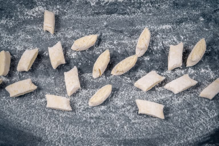 Slicing the flattened dough rope into small, diamond-shaped pieces with a knife.