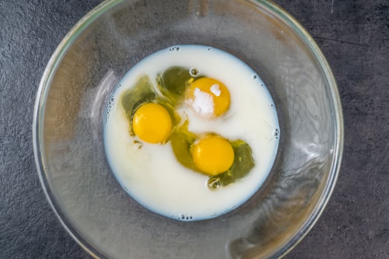 Whisking eggs, sugar, salt, and milk in a glass bowl to make crepe batter