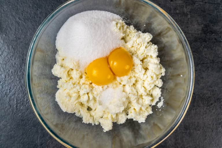 Combining dry-curd farmer's cheese, egg yolks, sugar, and vanilla in a bowl