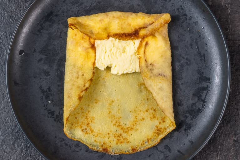 Tucking the left and right edges of the crepe inward over the cheese filling