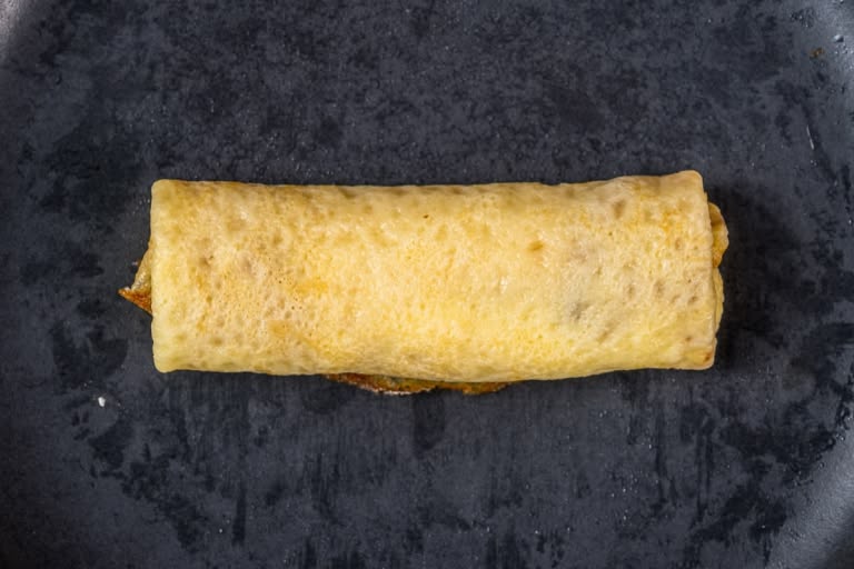Rolling the stuffed crepe upward into a neat envelope